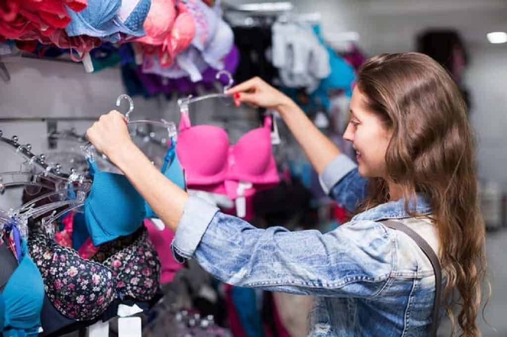 Woman in denim jacket holds up two bras for shopping
