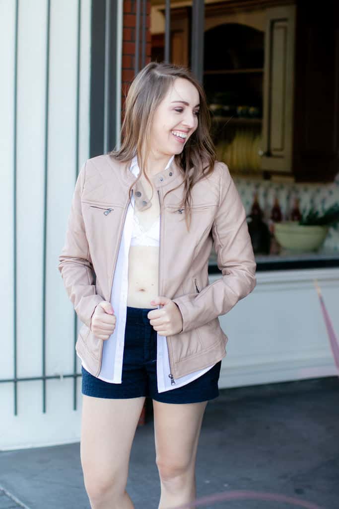 Woman wearing a tan jacket, white blouse and white bralette