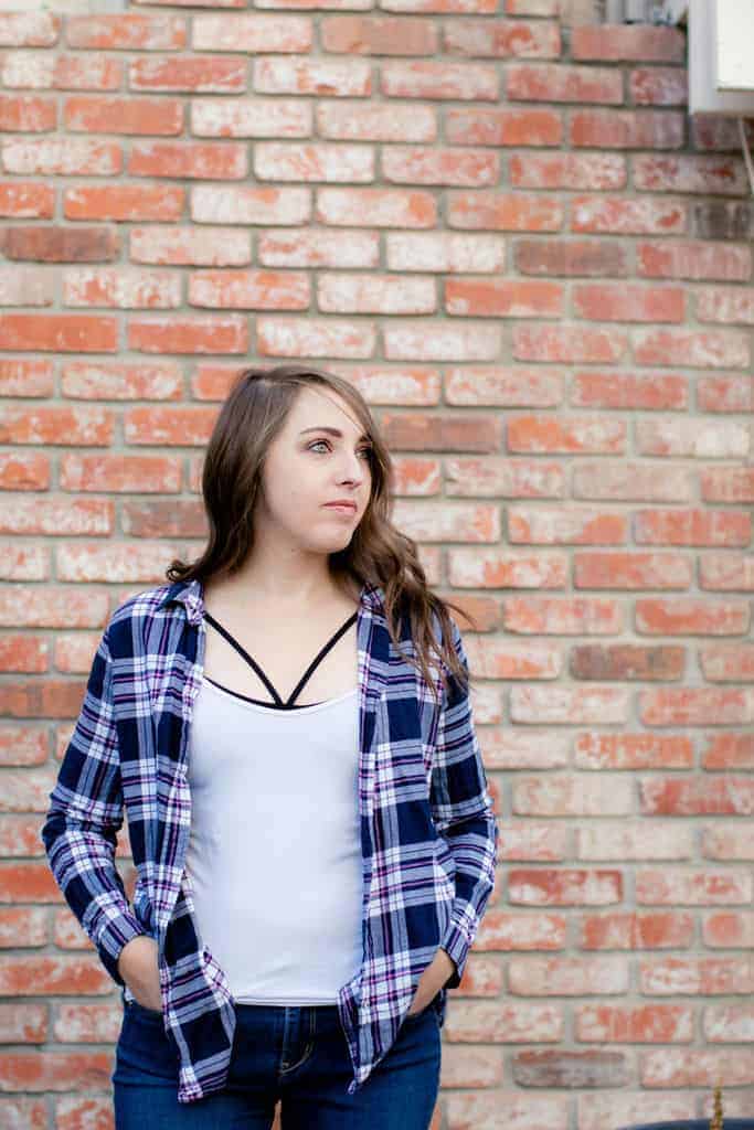 Woman wearing a strappy black bralette under white tank and plaid button down