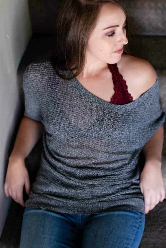 Woman wearing a dark red bralette underneath her gray shirt