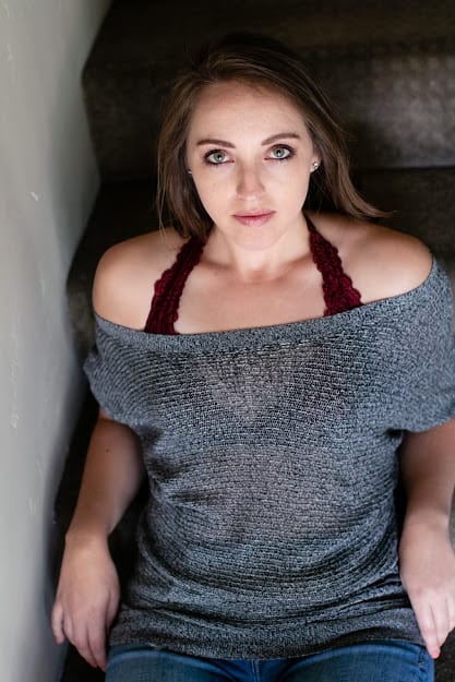 Woman wearing a gray off shoulder with her red bralette visible