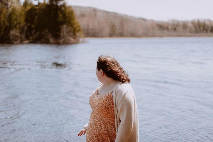 Woman wearing a flower printed dress with a cardigan while looking over a lake