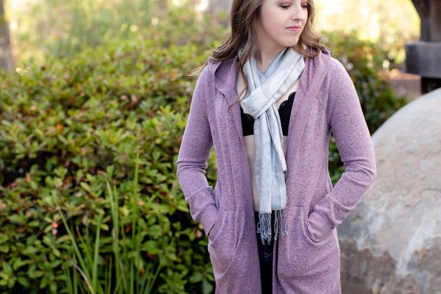 Woman wearing a purple long cardigan and black bra with a scarf wrapped in her neck