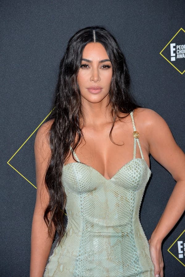 Kim Kardashian with long wavy hair wears a mint-colored snakeskin outfit with a low-cut neckline at an award show