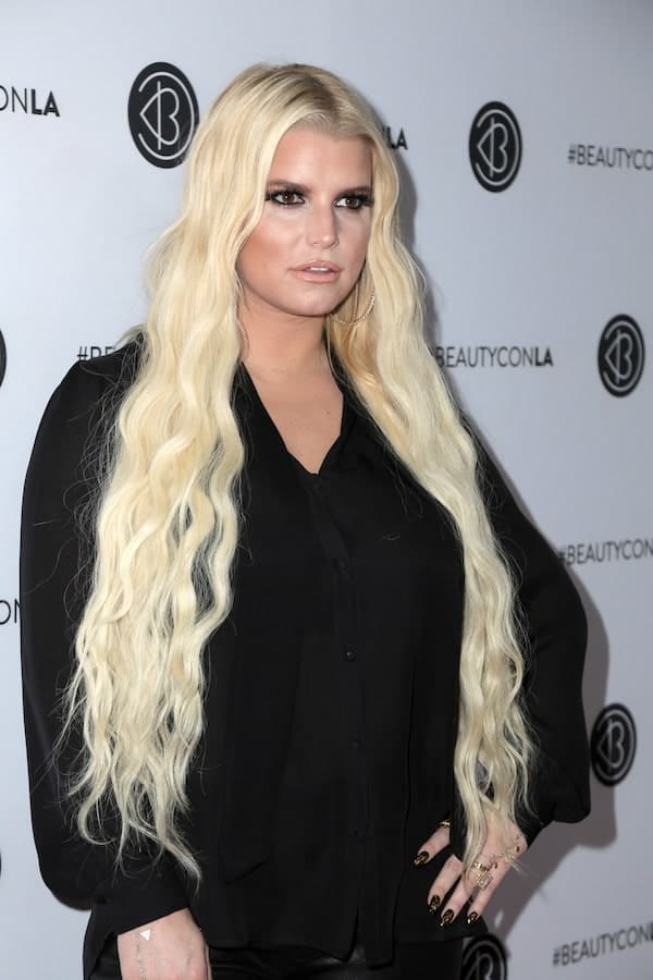 Jessica Simpson with long curly blonde hair wearing black long sleeves and black pants at a BeautyCon LA event