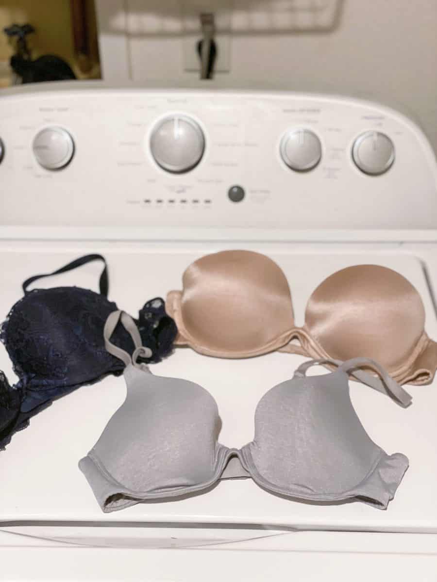 Three Victoria's Secret bras placed on top of a white washing machine in a laundry room