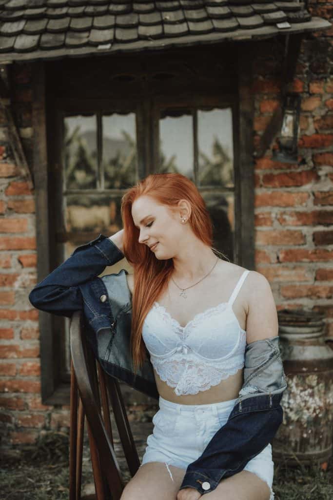 A girl in white bra sitting near a brick wall