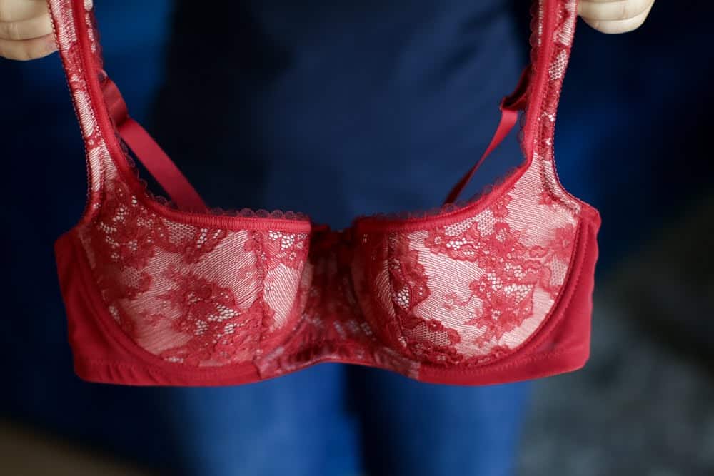 Person while standing holds a red balconette bra with a lace design