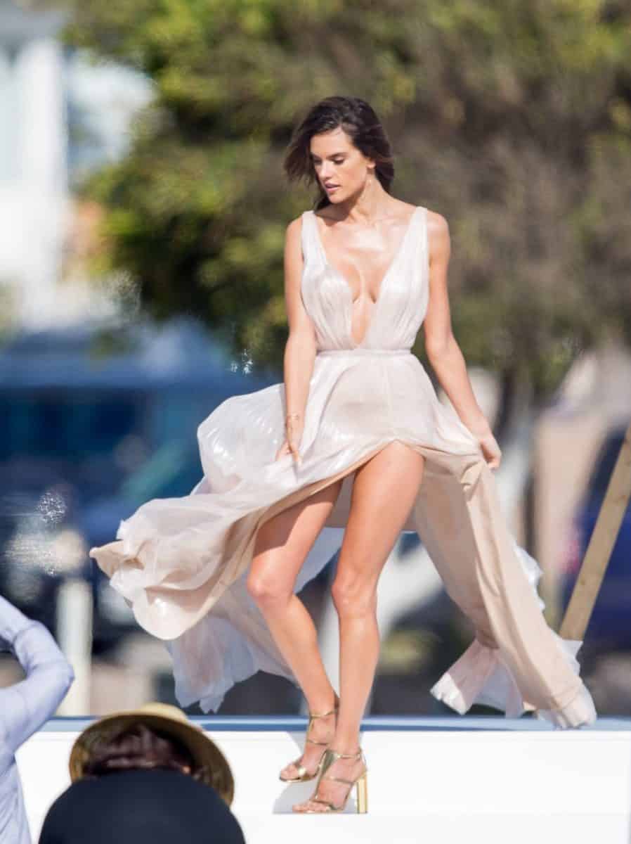 Alessandra Ambrosio wears a white pleated gown and a gold heels doing a photoshoot outside on a sunny day