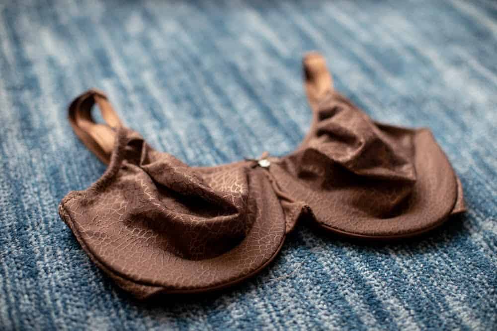 Brown minimizer bra with underwire and a wide center gore lying on a blue carpet