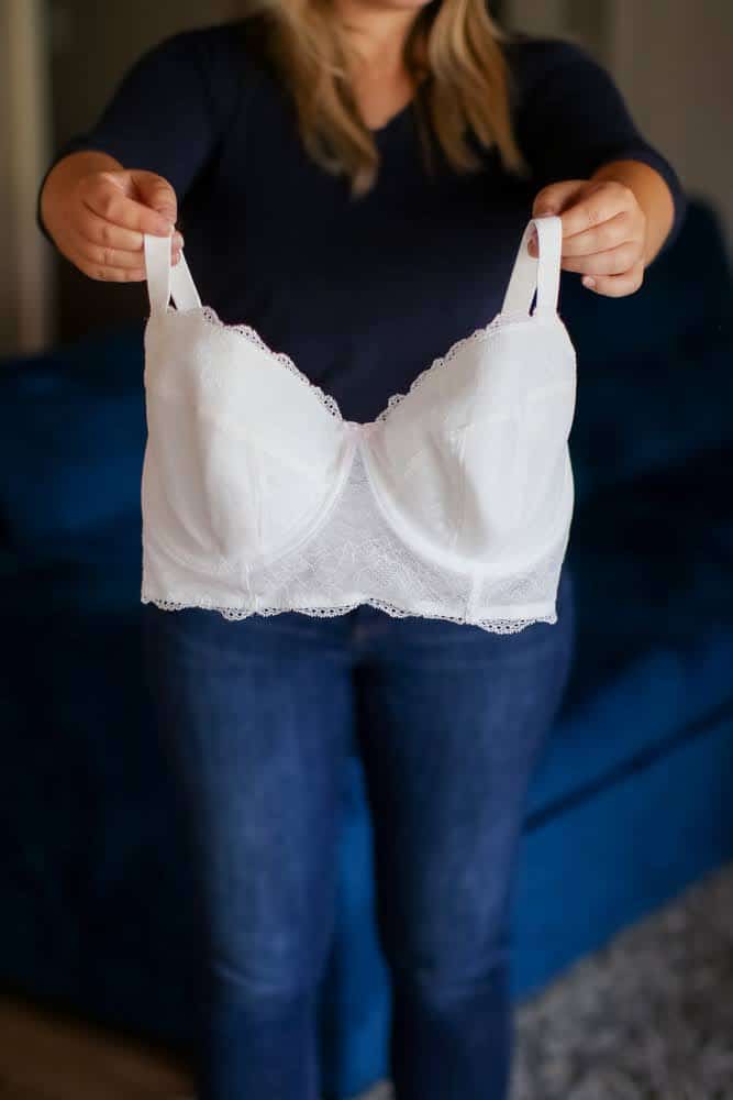 A person holds a white full-coverage bra standing near a blue couch in the living room