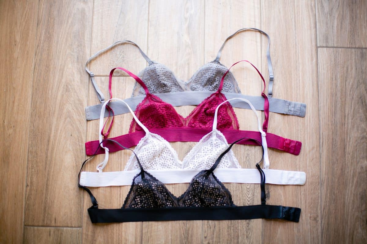 Four colors of v-neck bralettes piled up vertically on a brown wooden floor