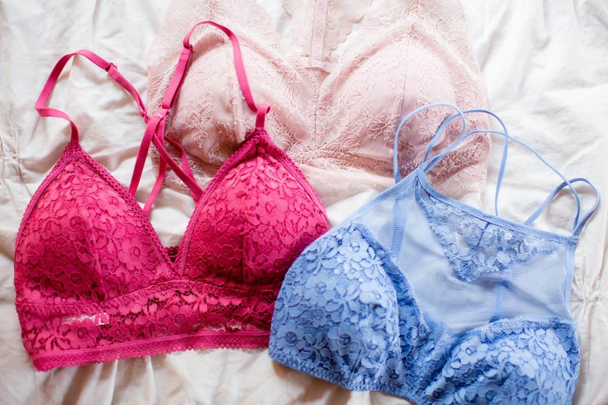 A pink v-neck bralette and a blue high-neck bralette and a light pink racer bralette were placed on the bed with a white bedsheet