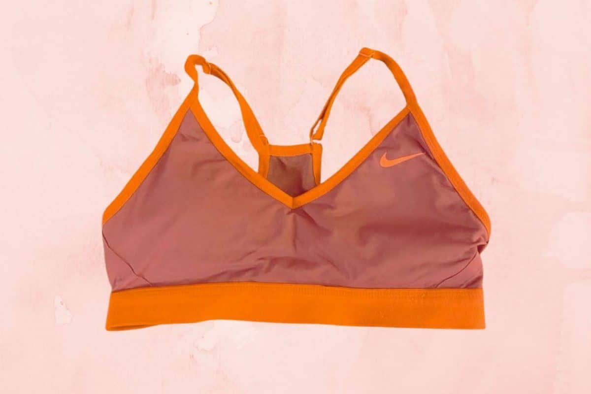 A purple Nike racerback sports bra is placed on a pink background