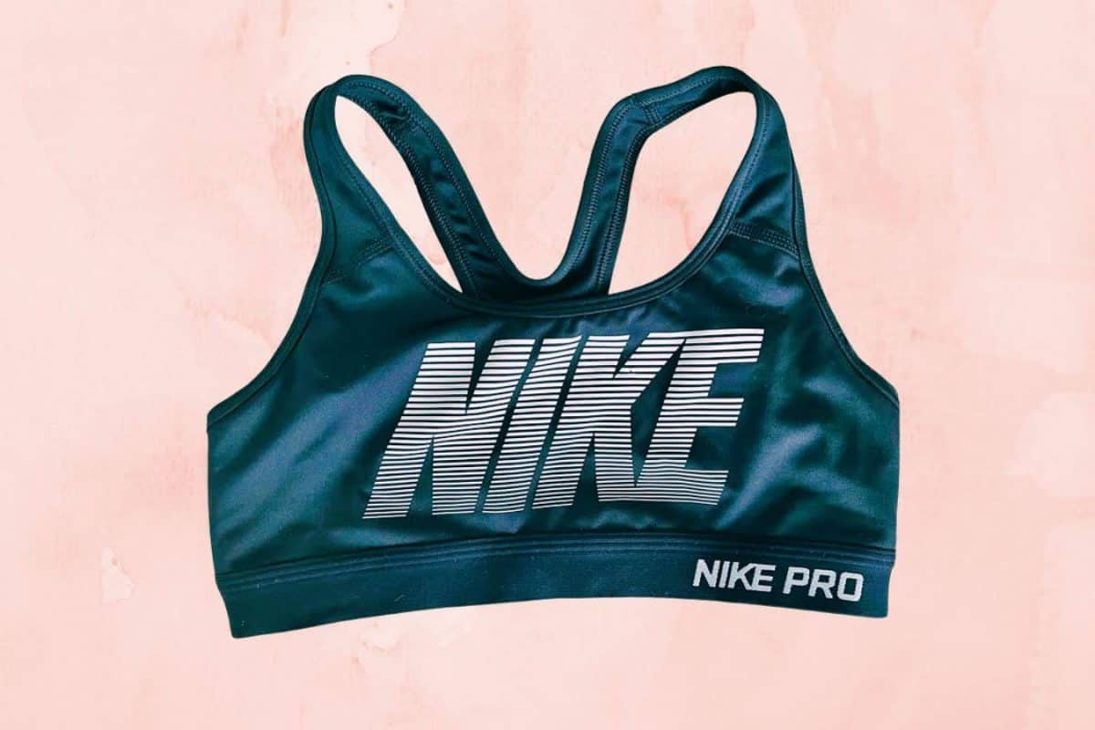 A blue-green Nike pro sports bra placed on a pink background