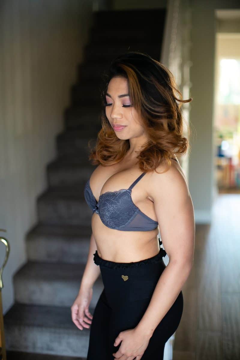 A woman wearing a gray push-up bra and black leggings standing near a staircase in the living room