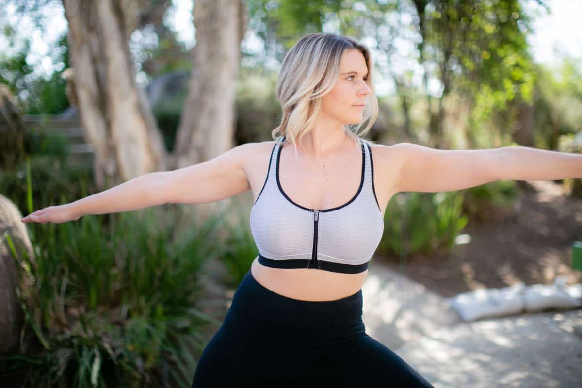 A woman in a gray zip-front sports bra and black leggings working out in the park