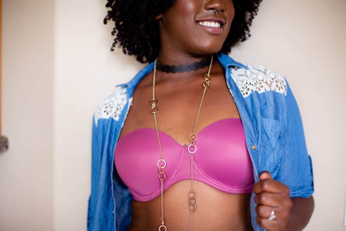 A woman in a pink underwire bra with a blue blouse stands near a white wall in the living room