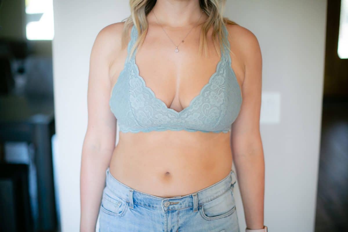 A woman in a powdered blue bra and blue jeans stands near a white wall