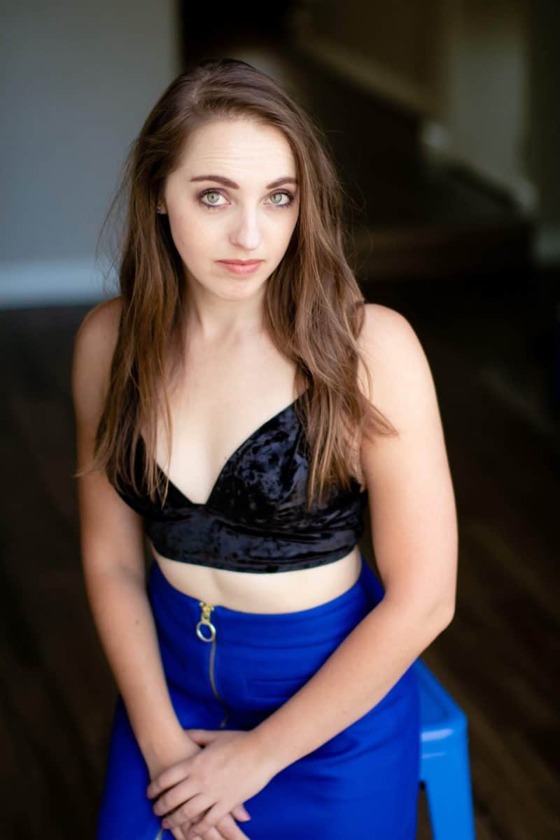 A woman wearing a black bralette and blue mini skirt is seated on a blue chair in the living room