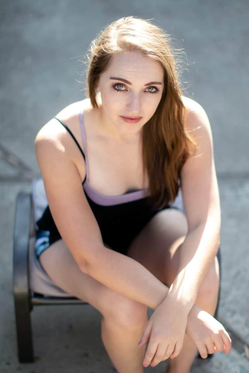 Black spaghetti strap tank top on top of purple bralette worn by a woman seated on a stainless chair
