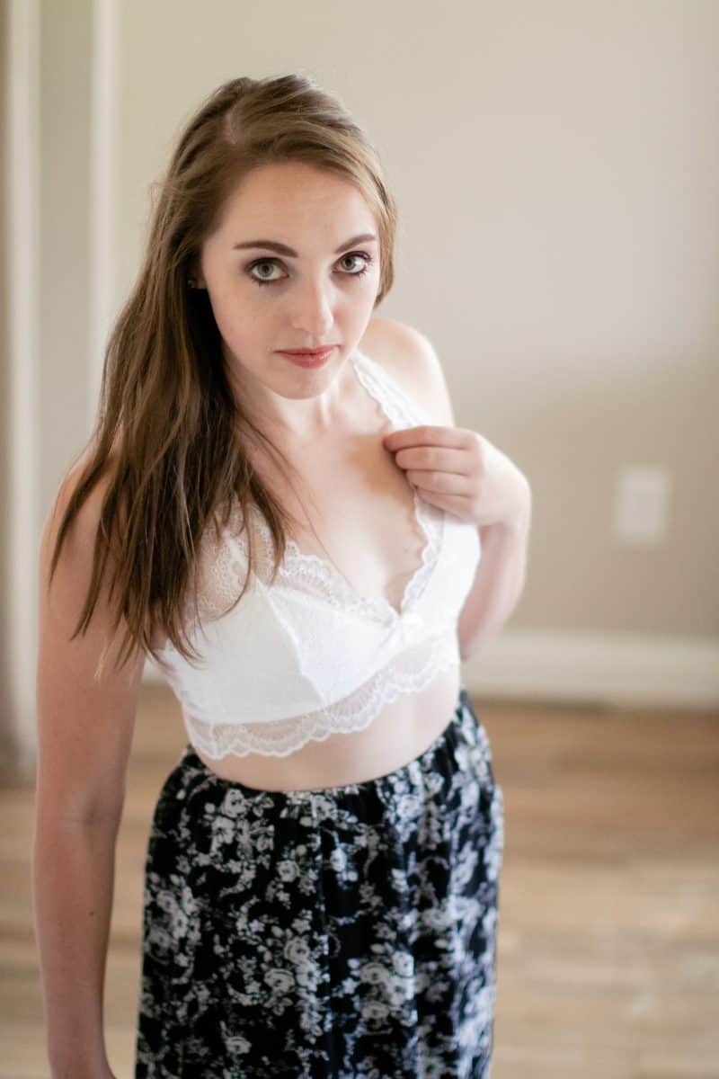 A white lace bralette and skirt with a flower design worn by a woman standing near a white wall