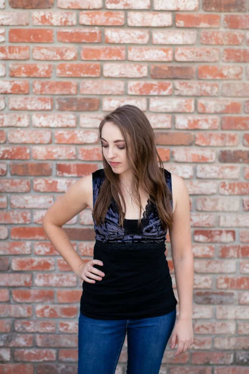 A black blouse and blue denim jeans worn by a woman standing near a brick wall