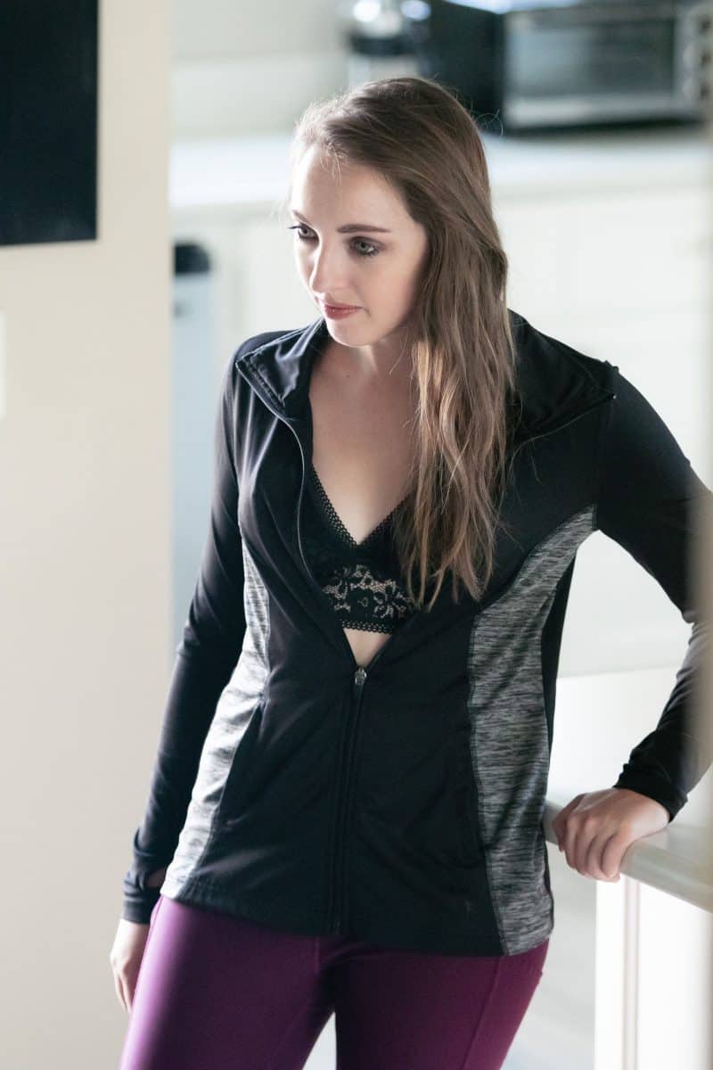 A black bralette and black jacket was worn by a woman leaning on a white tabletop