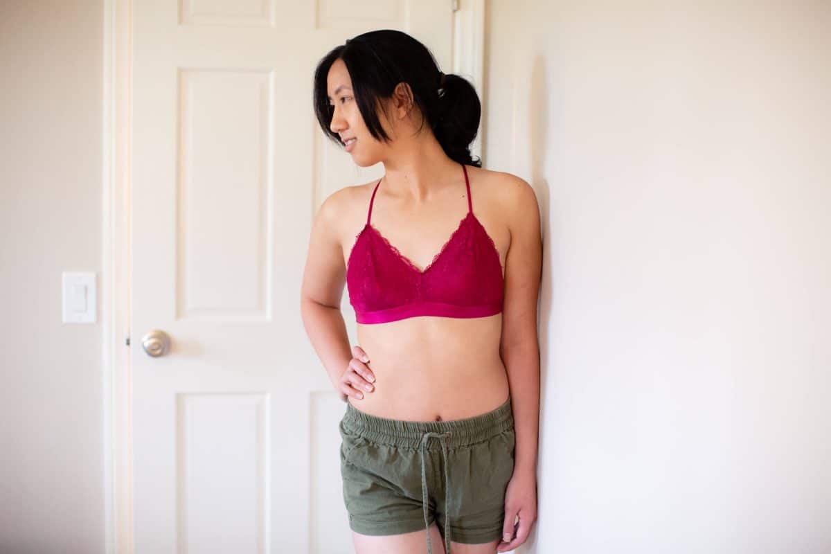 A woman is wearing a pink bralette and green shorts standing near a white door in the living room