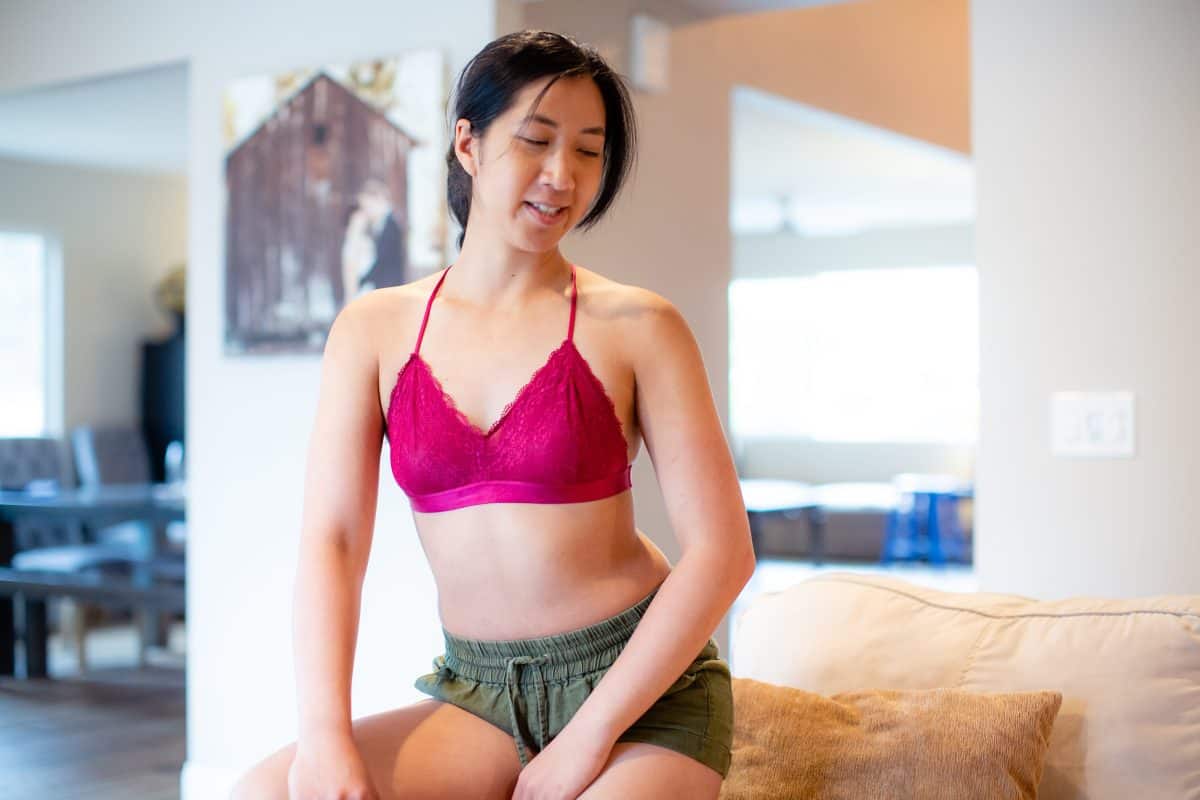 A woman is wearing a pink bralette and green shorts seated on a yellow couch in the living room