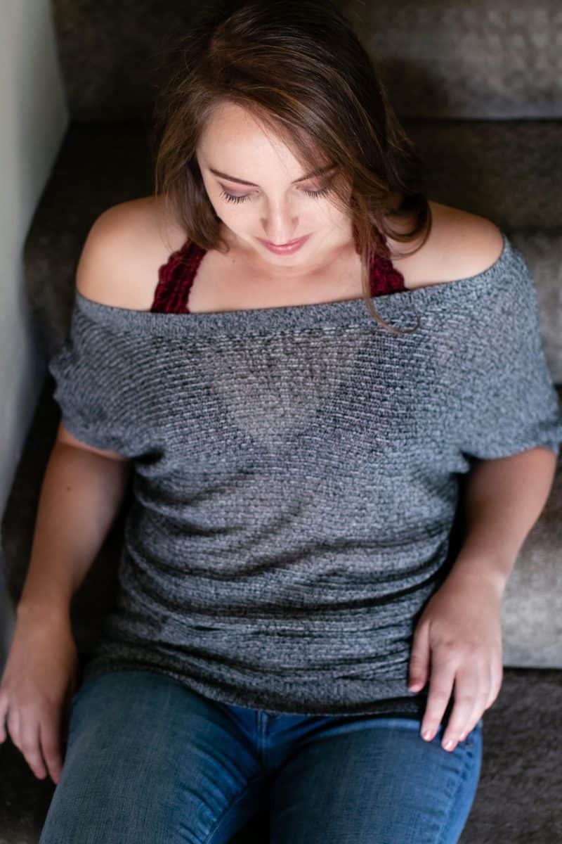 A top view of a woman wearing a gray off-shoulder shirt and blue denim jeans seated on the stairs