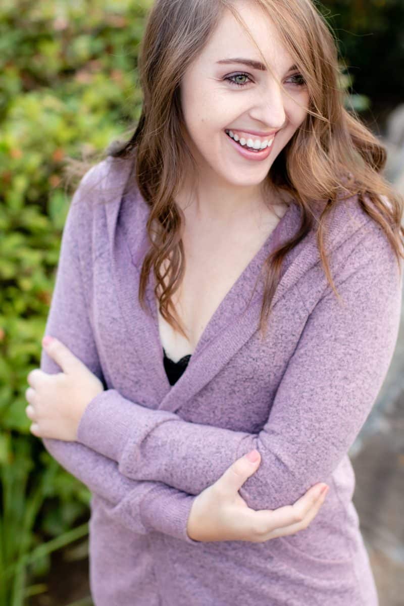 A woman wearing purple long sleeves and a black bralette is standing near a plant in the park