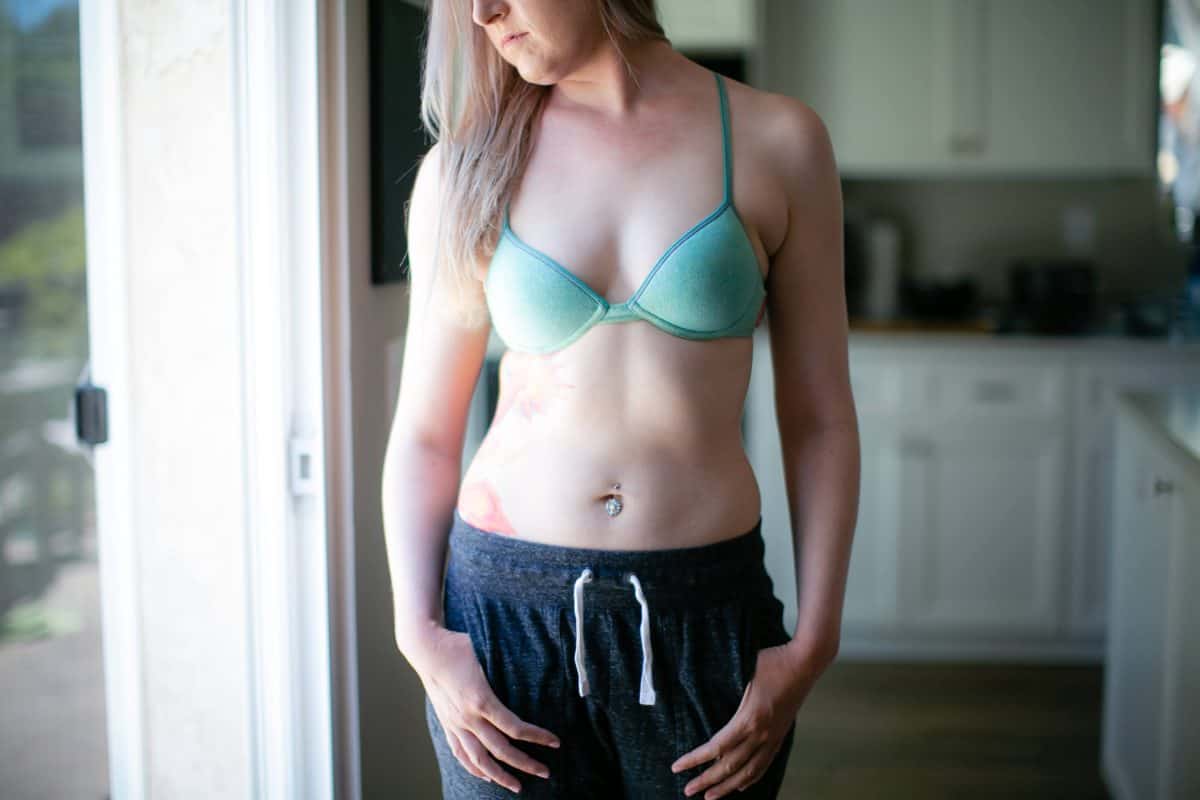 A woman wearing a green bra with underwire and black jogging pants standing in the kitchen