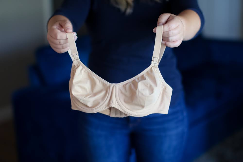 Woman holding a cream underwired nursing bra with adjustable wide straps