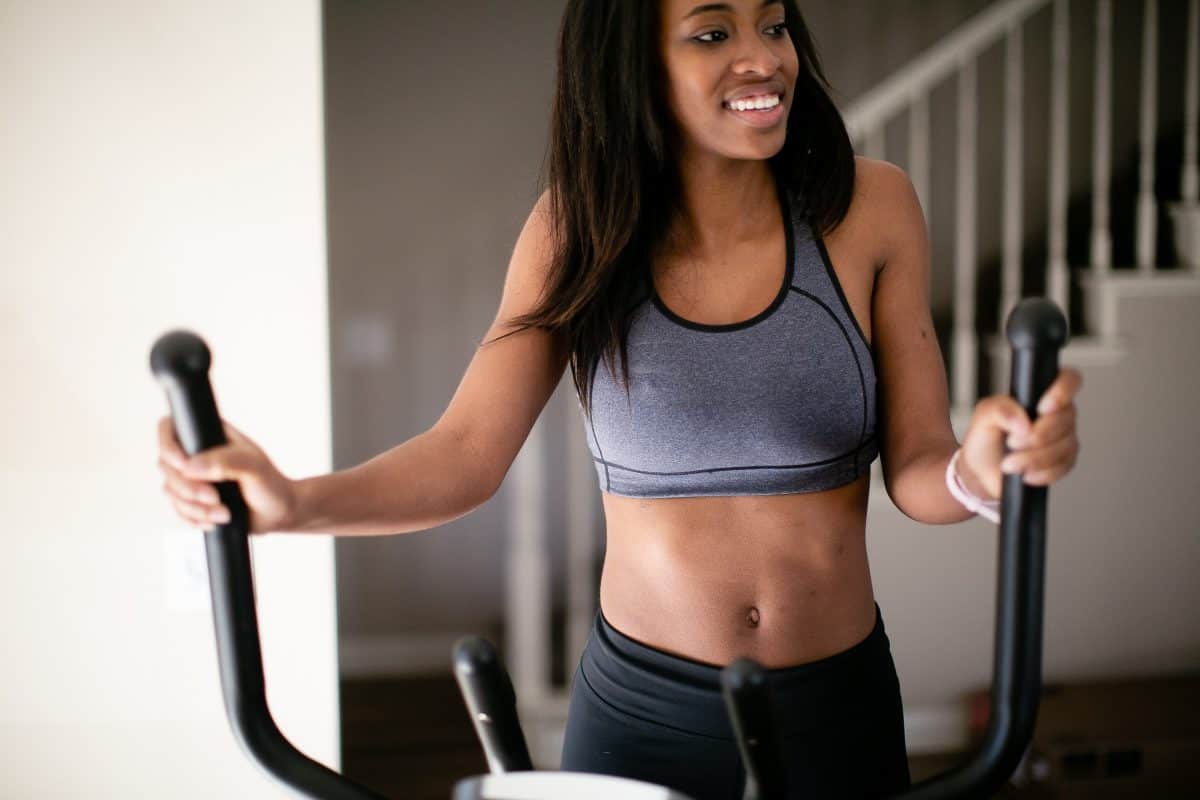 Woman in a black sports bra and black leggings using an elliptical machine in the house