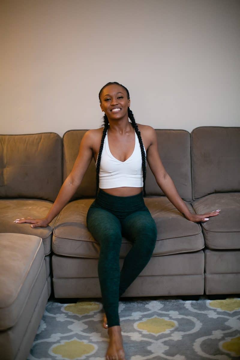 White unpadded bra and green leggings are worn by a woman seated on a brown couch