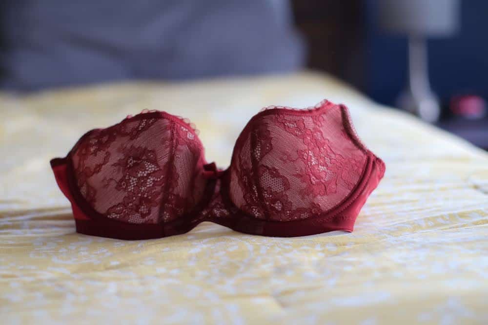 A red lace balconette bra with an underwire placed on a yellow bedsheet
