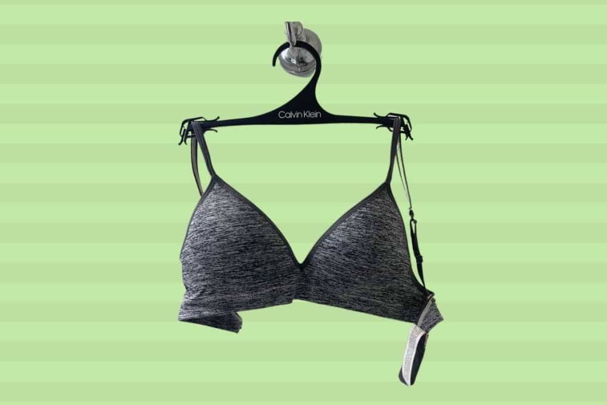 A black Calvin Klein wireless bra placed on a hanger on a green background