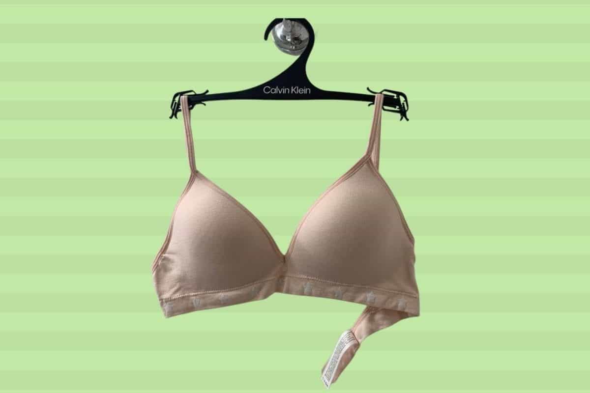 A cream wireless bra placed on a Calvin Klein hanger on a green background