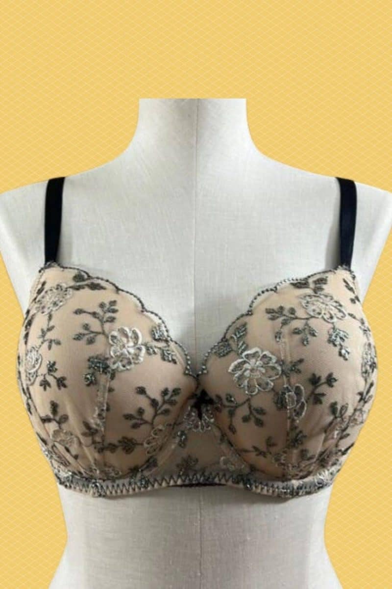 Cream full coverage bra with black straps and a flower design placed on a mannequin