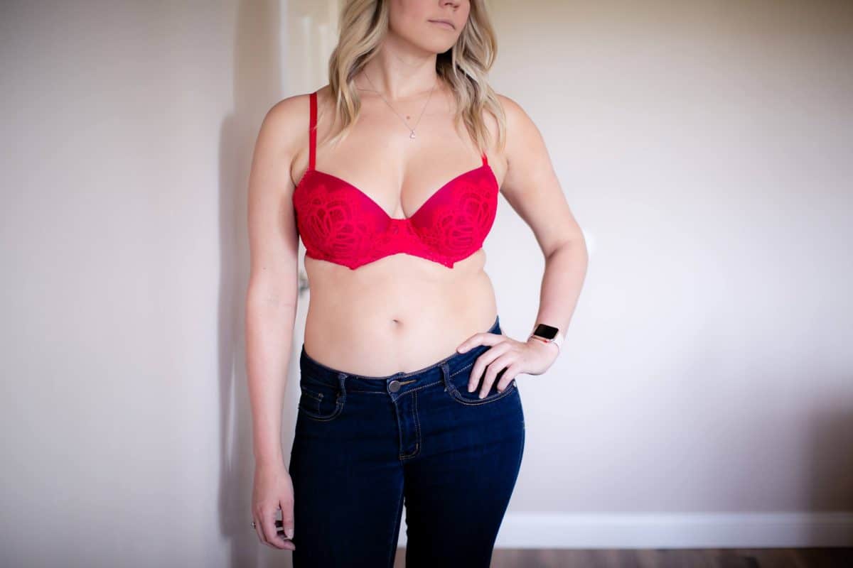 A woman wearing a pink push-up bra and denim jeans standing near a white wall