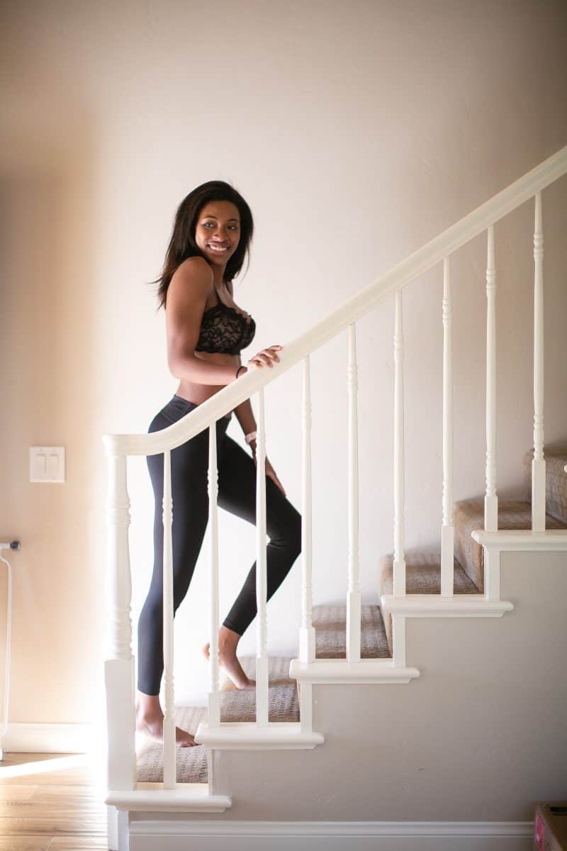 A woman in a black balconette bra and black leggings is walking up the stairs