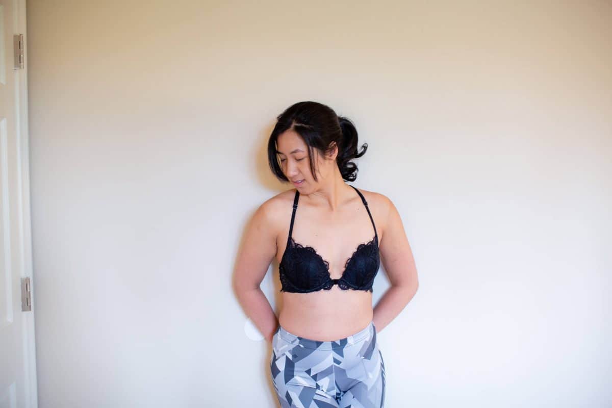 A young woman wearing a black racerback bra and leggings leaning on a white wall