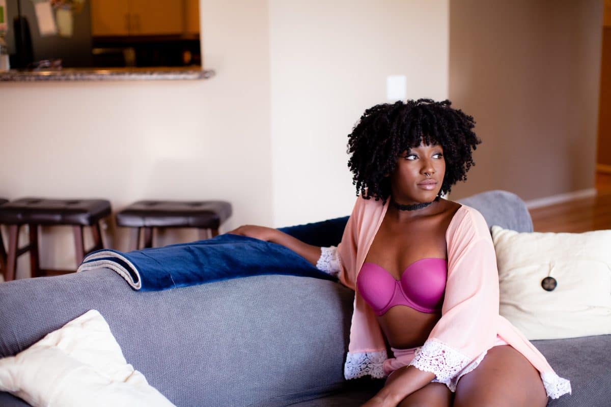 A woman wearing a pink strapless bra and cardigan is seated on a gray couch