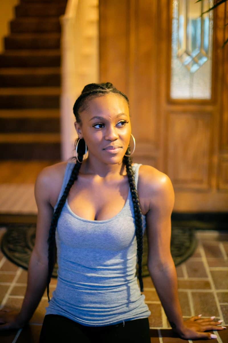 Woman wearing a gray tank top and black leggings seated on ceramic tiles