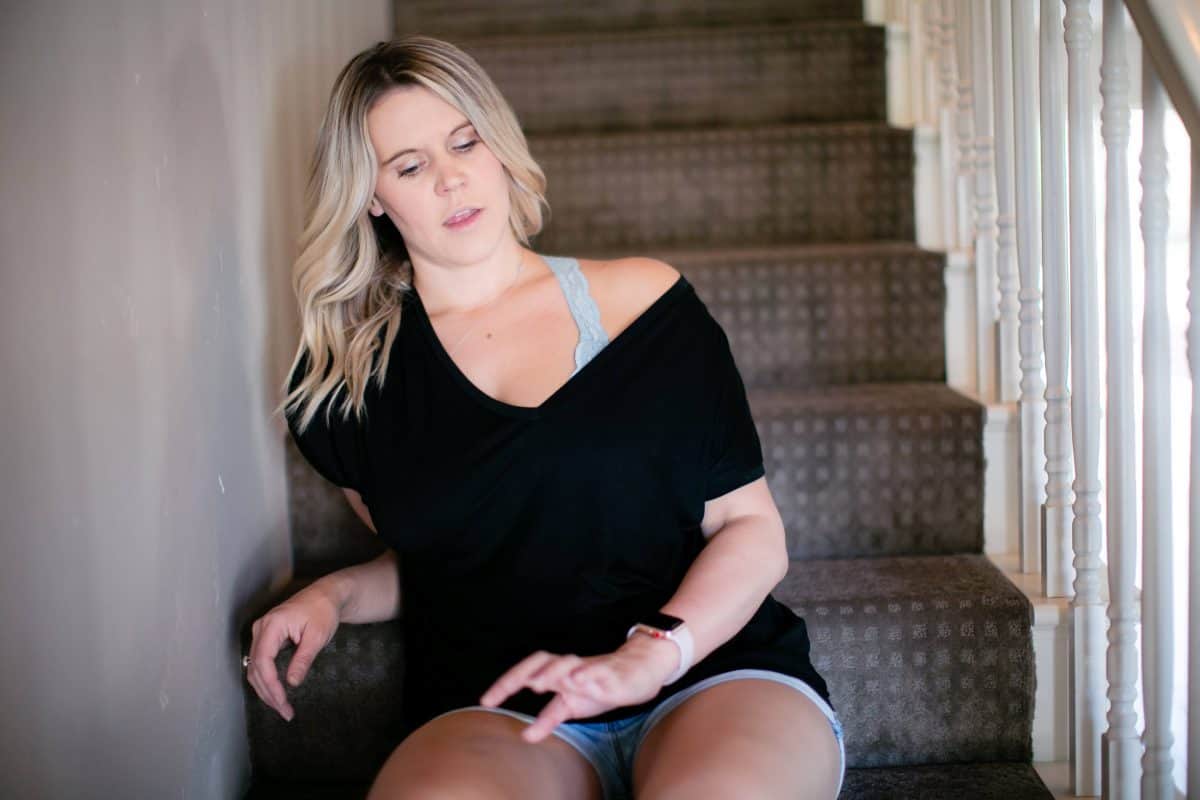 A woman wearing a black one off shoulder top and denim shorts seated on the stairs