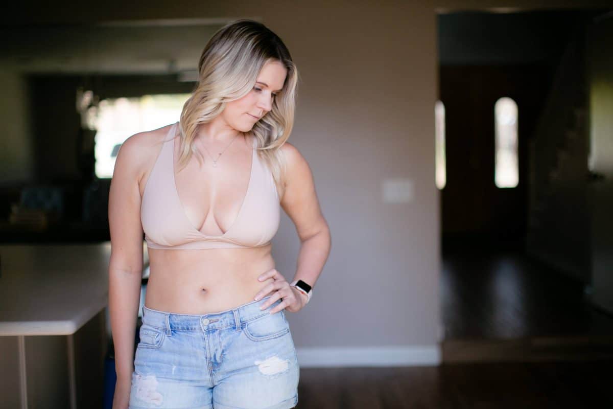 A nude wireless bra and denim shorts are worn by a woman wearing a smartwatch
