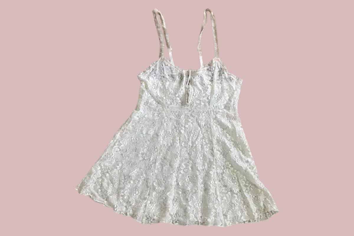 A white spaghetti strap Teddy lingerie with a floral lace design placed on a pink background