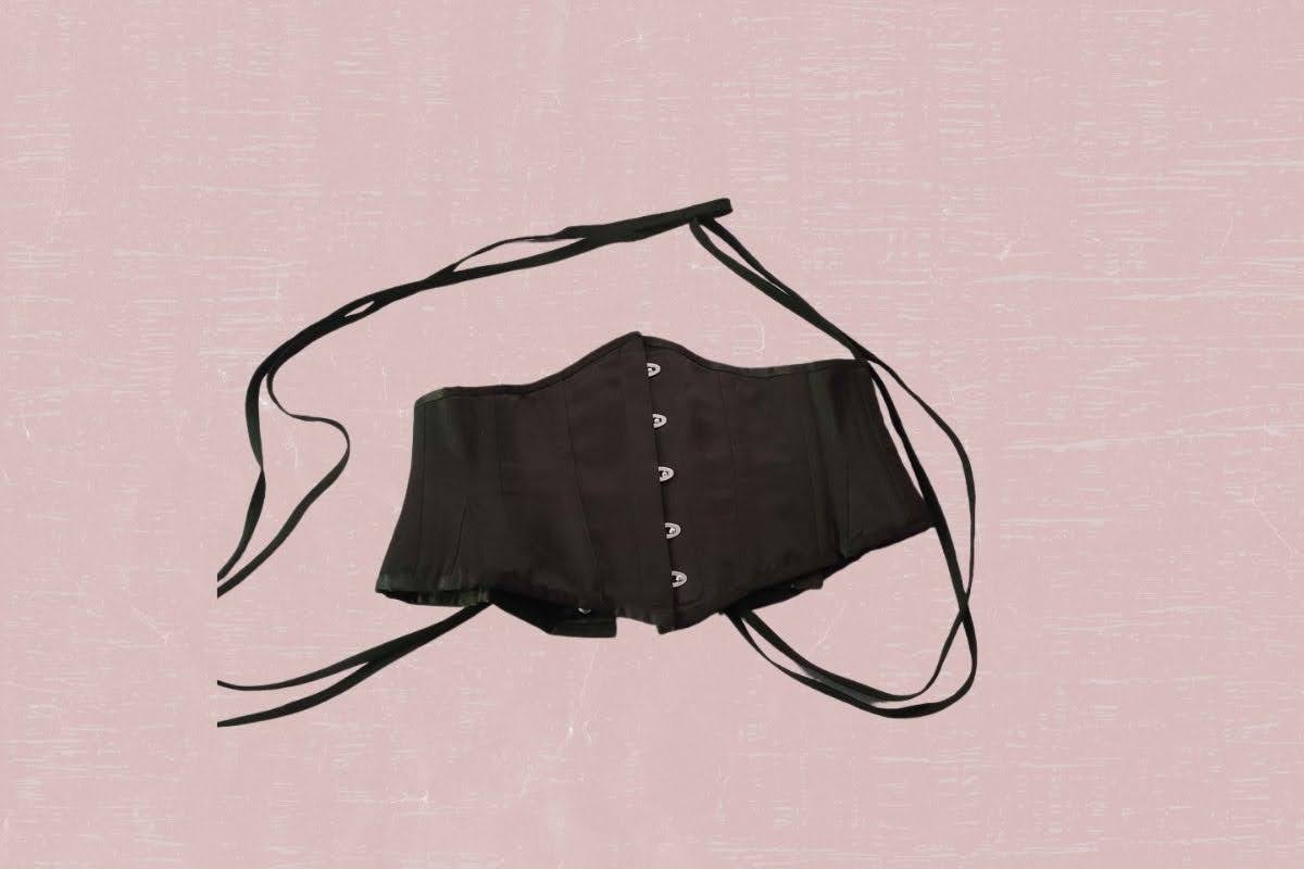 A black waspie with black strings and hooks was placed on a pink background