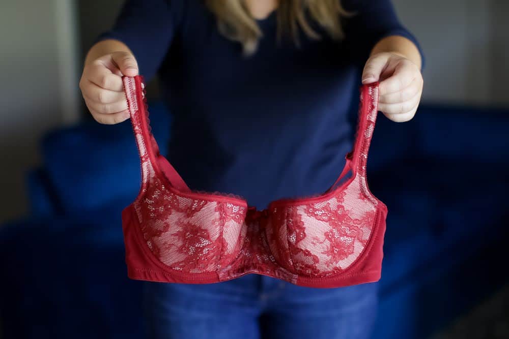 A red balconette underwire bra with a lace design holds by a woman wearing a blue t-shirt and denim jeans